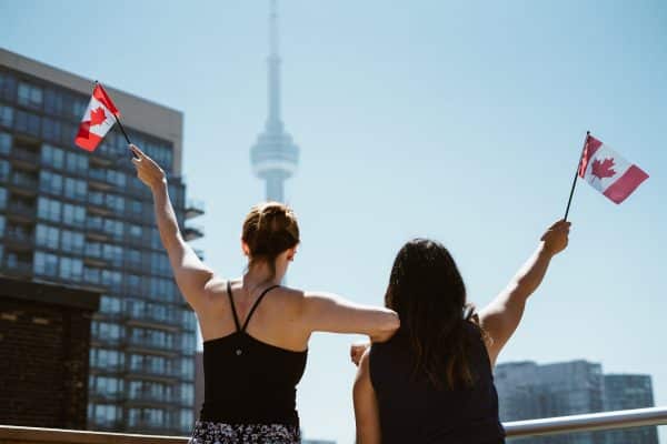 Deux étudiantes avec des drapeaux canadiens aux mains posant devant la célèbre tour de Toronto